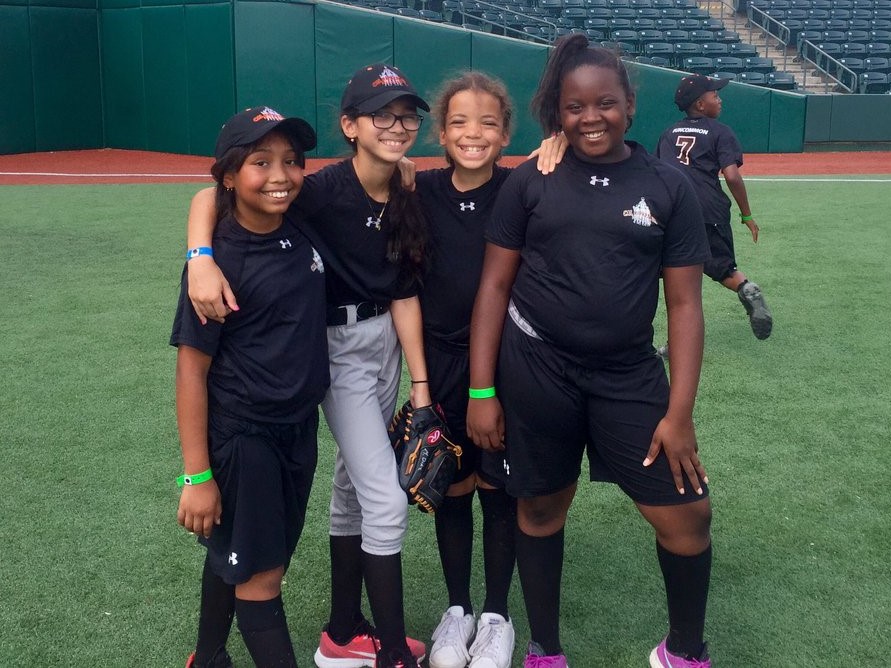Four girls in black on a baseball field.